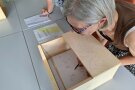 Person sitzt vor Holzaufbau auf einem Tisch.