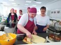 Studierende streicht Tortenboden ein, weitere Personen stehen dahinter