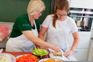 2 Frauen stehen an Arbeitsplatte in Küche hinter Schüsseln mit Gemüse