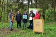 Mehrere Personen posieren mit einer Urkunde und einer Holzskulptur