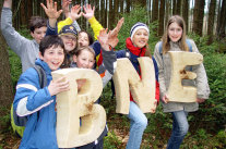 Kinder im Wald, die die aus Holz gesägten Buchstaben B, N und E halten