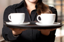 Frau trägt zwei Kaffeetassen auf einem Tablett